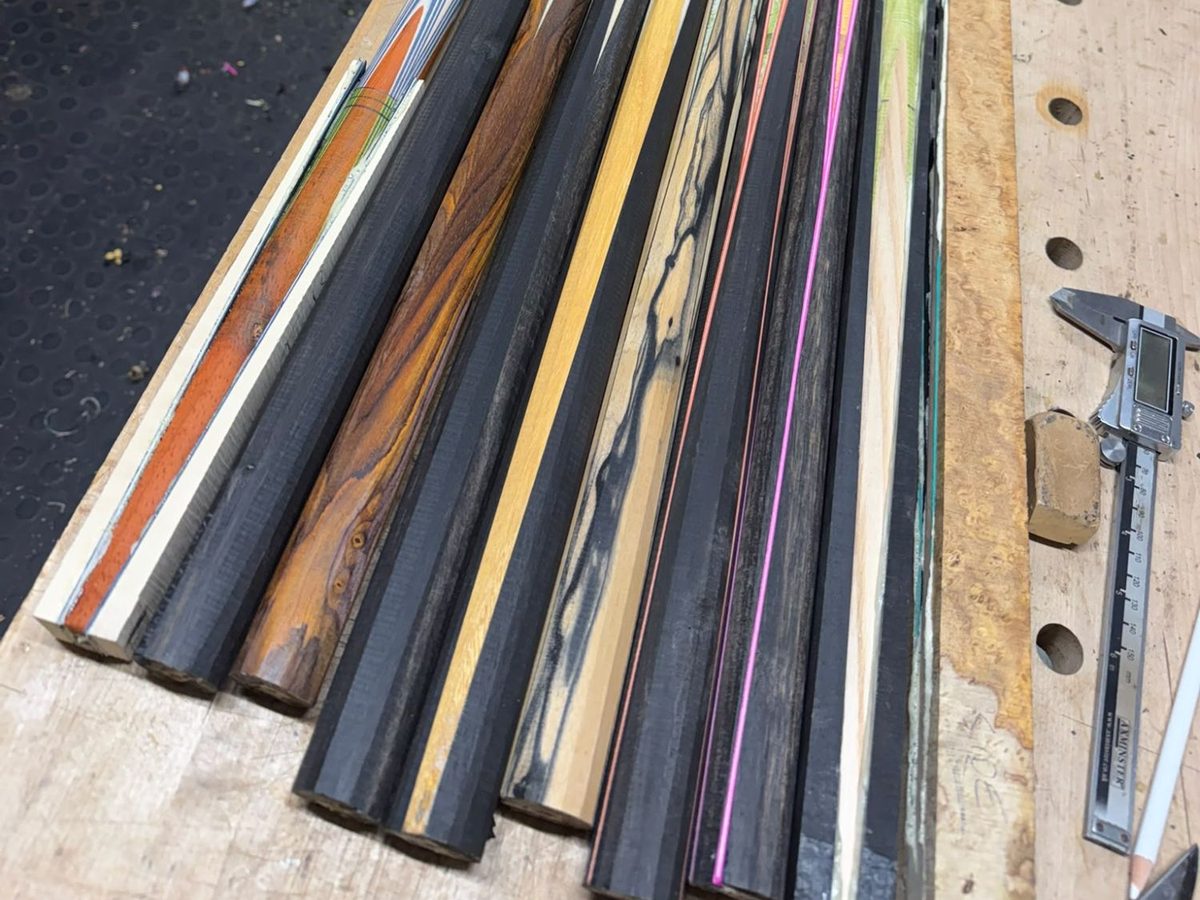 Row of part-finished cue butts in black, rich brown and striped veneers with orange and pink inlay lines, beside digital callipers