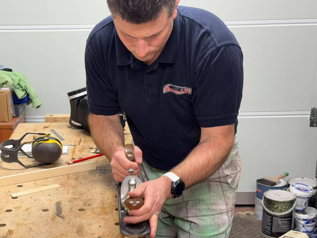 Cue maker hand-planing a pool cue shaft with a bench plane at a workshop bench
