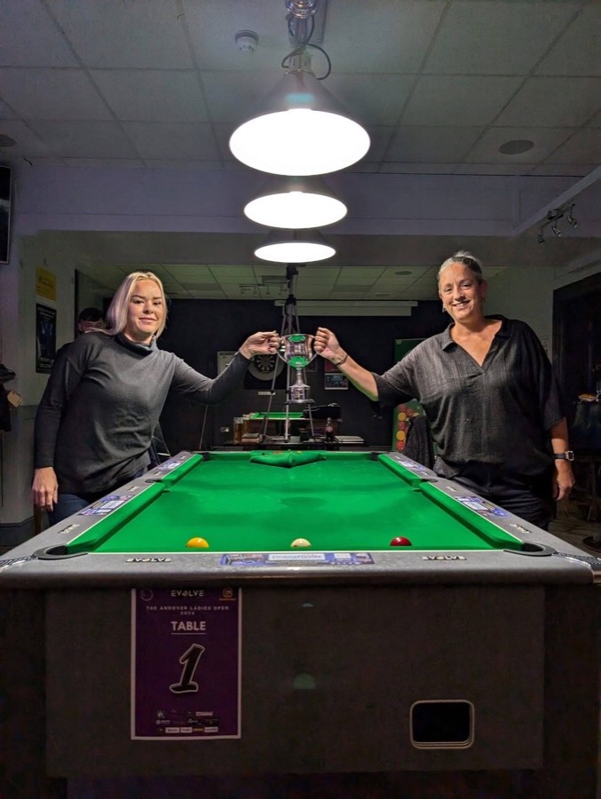 Two finalists holding the Andover Ladies Open trophy above table one before the final at an Evolve event