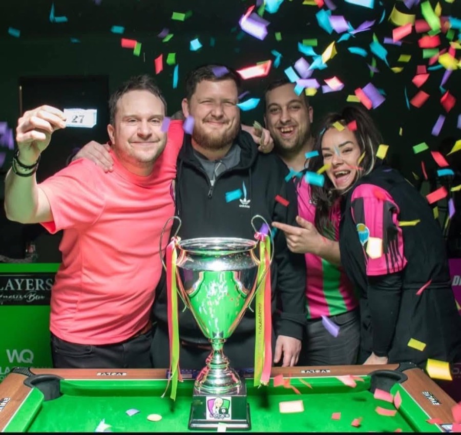 Winning team lifting the Lola's Pool Party trophy under falling confetti beside the table at the Wolversdene Club